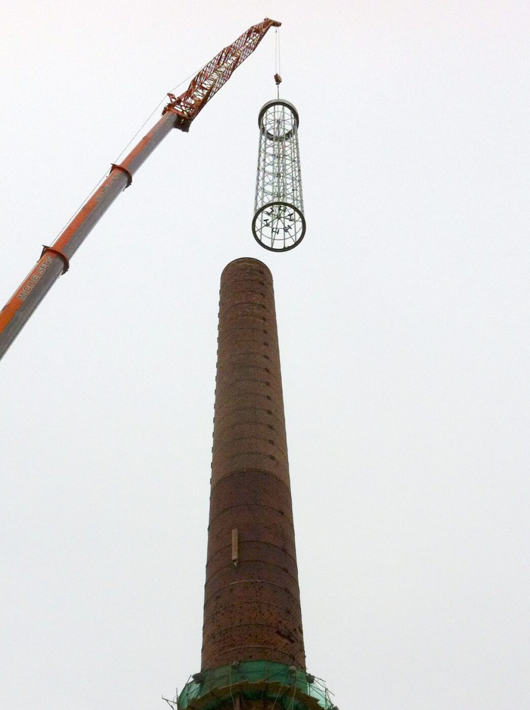 Een kraan hijst in één keer de 15 meter staalconstructie op de schoorsteen